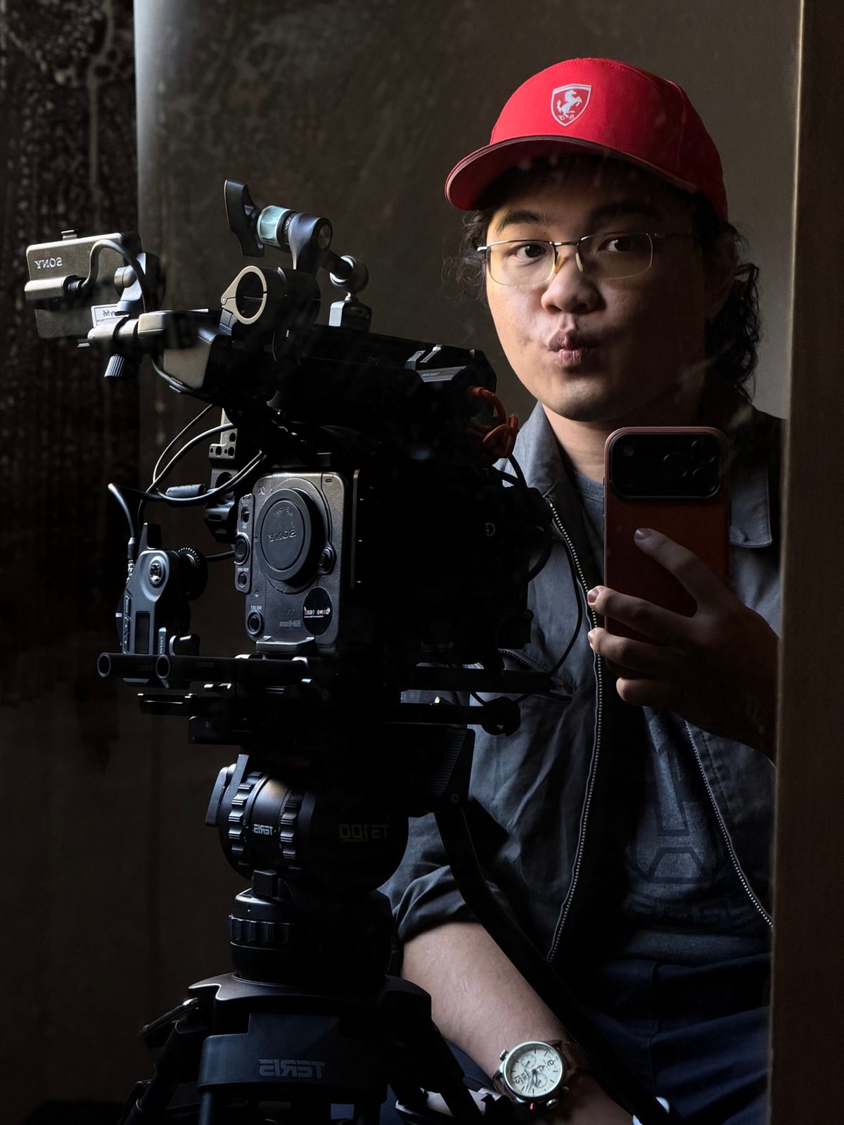 Krit behind a cinema camera rig, red cap, phone in hand