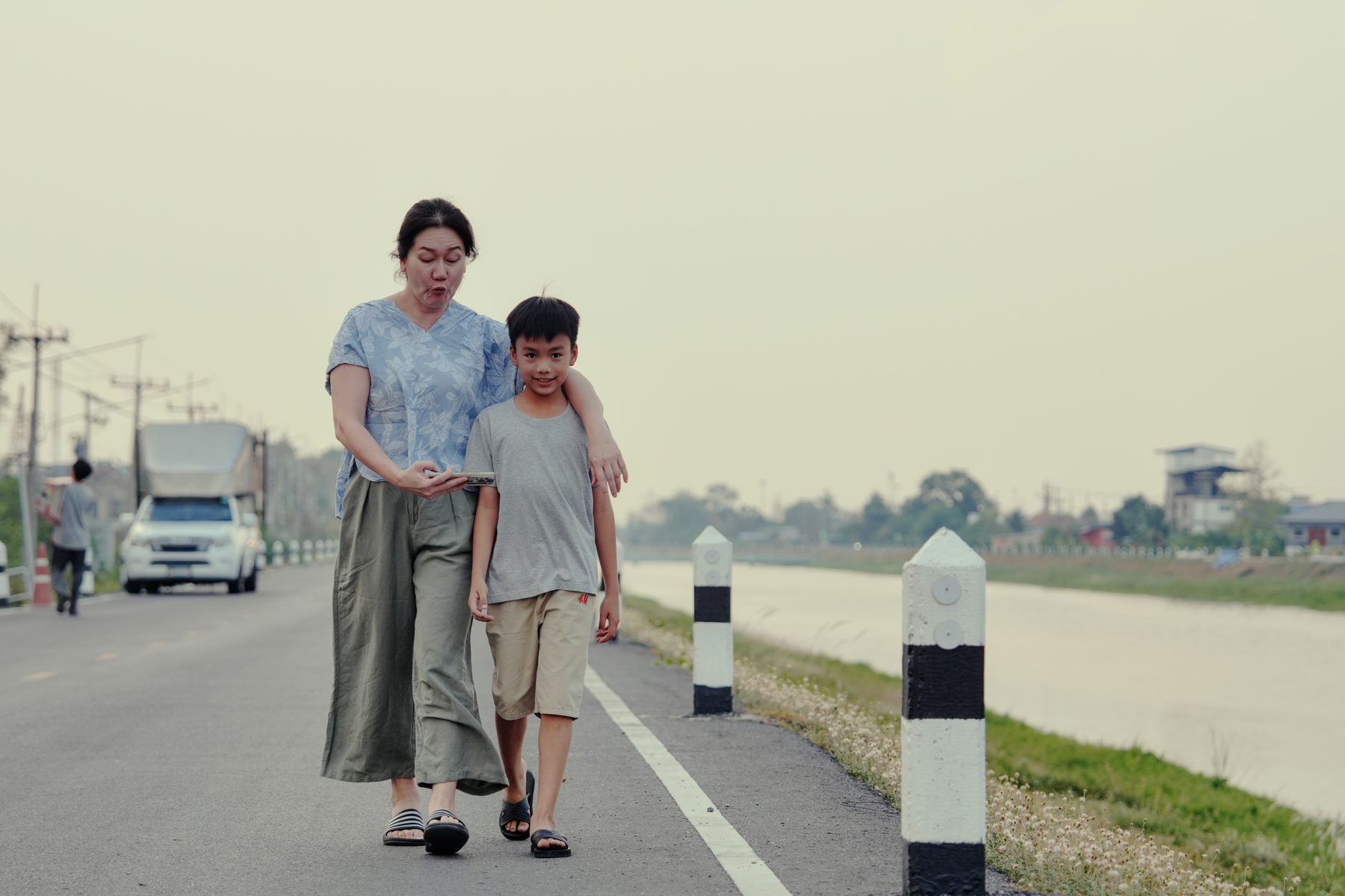 A mother walks her son along a canal road, her arm around his shoulders