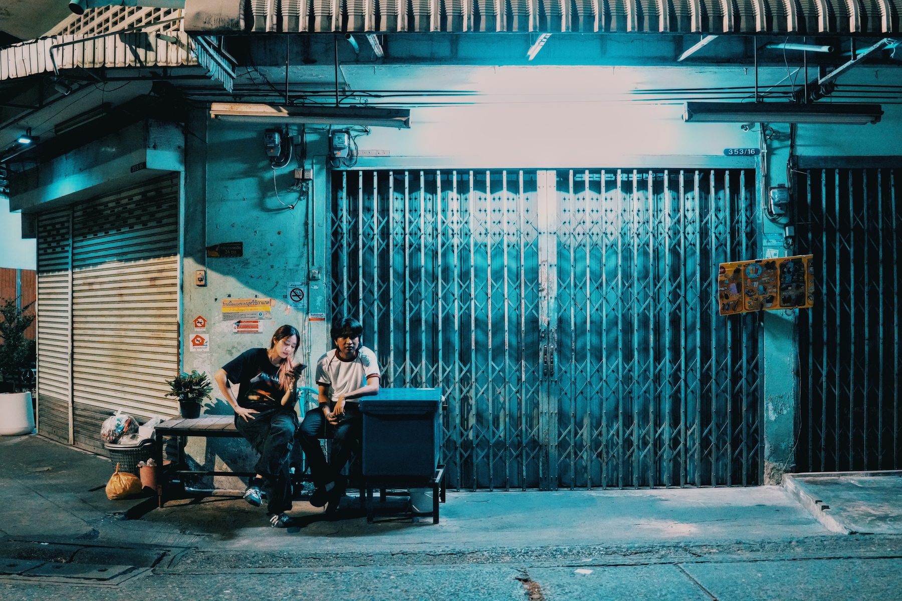A woman sits in front of a shuttered shophouse at night