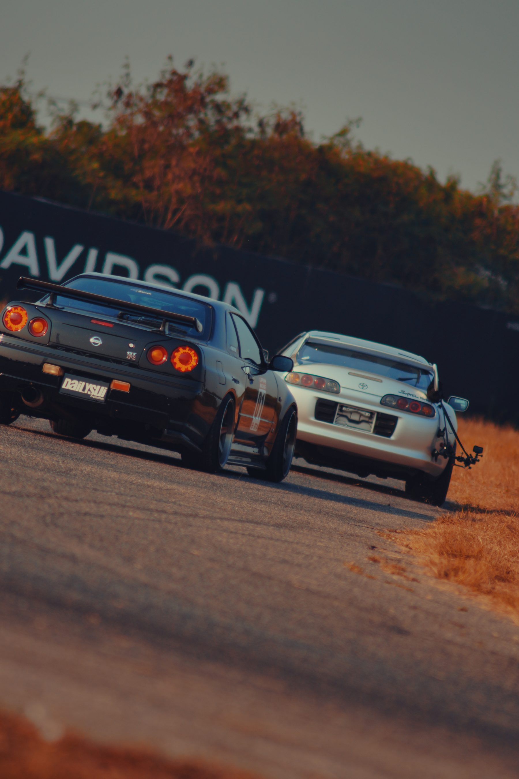 Two classic Japanese sports cars on an open road in low sun
