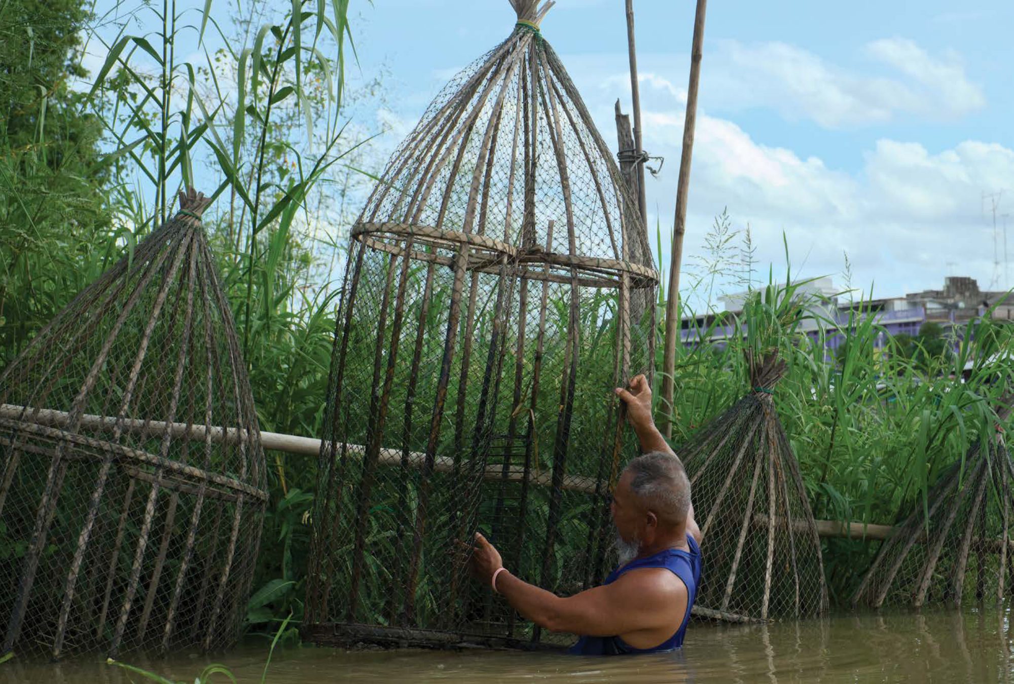 Sinthuchai lifts a large wicker fish trap beside his raft house on the Sakae Krang river
