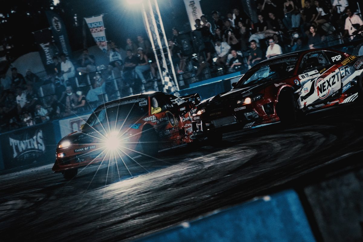 Tandem drift under the floodlights — two cars side by side through the smoke